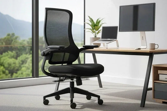 Black ergonomic mesh office chair in NZ beside a modern desk with monitor and laptop in a bright home office.