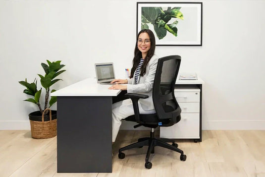 A woman at a corner desk in a compact commercial area, engaged with her laptop.