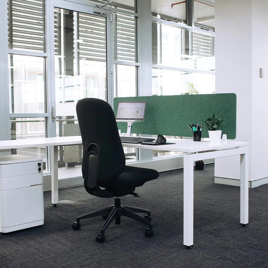 A modern white office desk setup with a black swivel chair, a green privacy screen, and a white storage cabinet in a bright, contemporary office space.