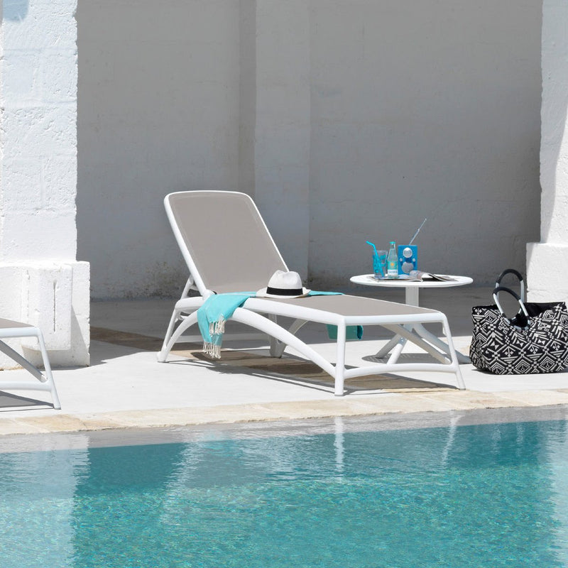 Load image into Gallery viewer, White lounge chair by a pool with a table and items on it.
