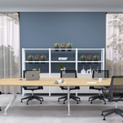 Modern office setup with a long wooden table and black chairs in front of a blue wall.