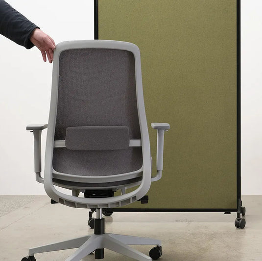 Gray office chair being adjusted by a person with a white wall and green partition in the background.
