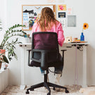 Person sitting at a desk in a home office with a plant and decorative items.