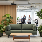 Modern office space with a green sofa, wooden coffee table, and potted plants.