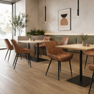 A modern dining room setup featuring brown upholstered chairs with black metal legs, rectangular light wood tables with black bases, and a green upholstered wall seat along a beige wall with abstract wall art.