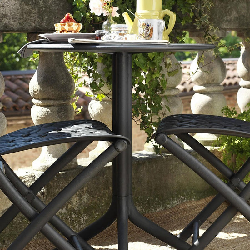 Load image into Gallery viewer, Outdoor setting with a black metal table and chairs, surrounded by greenery and stone architecture.
