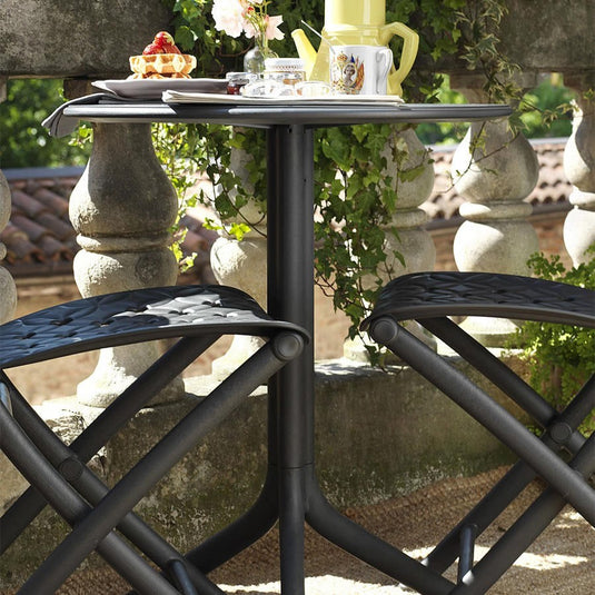 Outdoor setting with a black metal table and chairs, surrounded by greenery and stone architecture.
