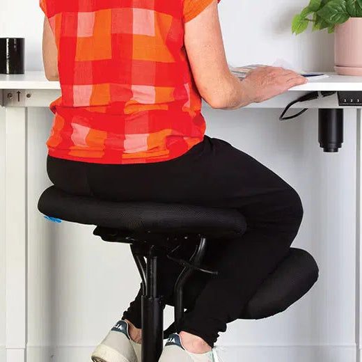 Person sitting on a black office chair at a white desk with a plant and mug in the background.