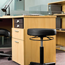 Wooden office desk with a black swivel stool in an office setting.