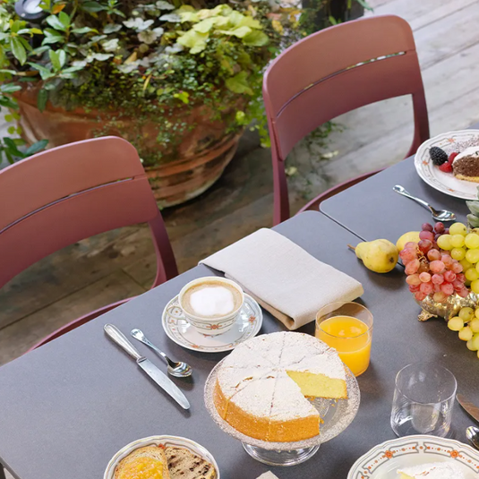 Outdoor dining table with food, drinks, and chairs on a patio.