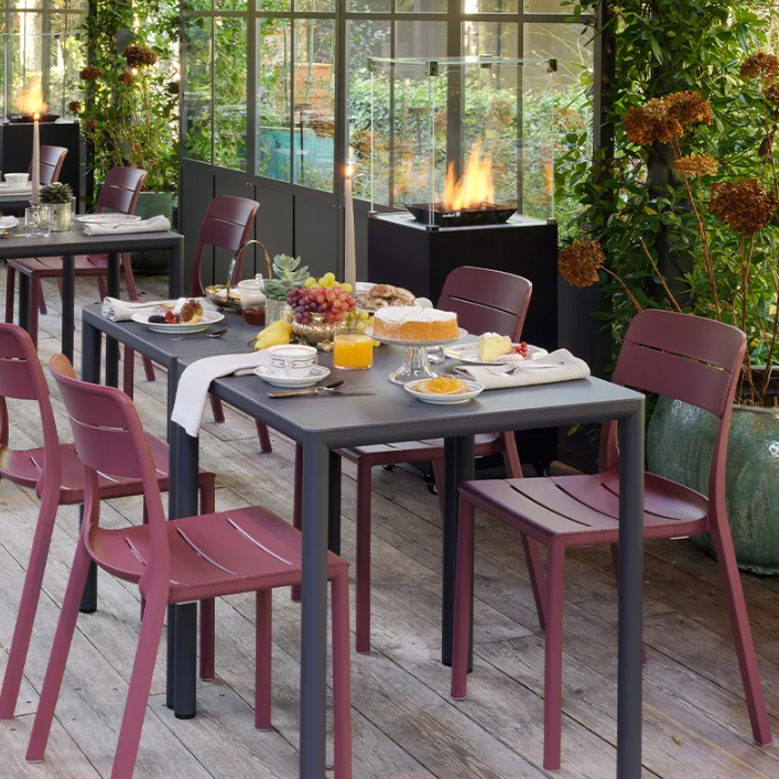 Load image into Gallery viewer, Outdoor dining area with tables and chairs on a wooden deck, surrounded by greenery.
