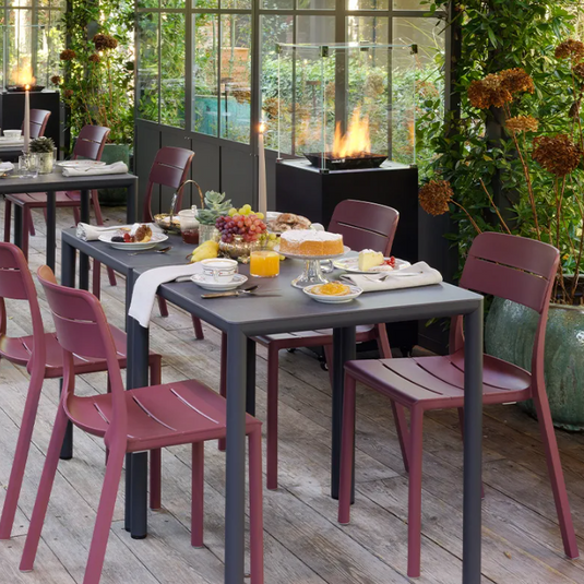 Outdoor dining area with tables and chairs on a wooden deck, surrounded by greenery.