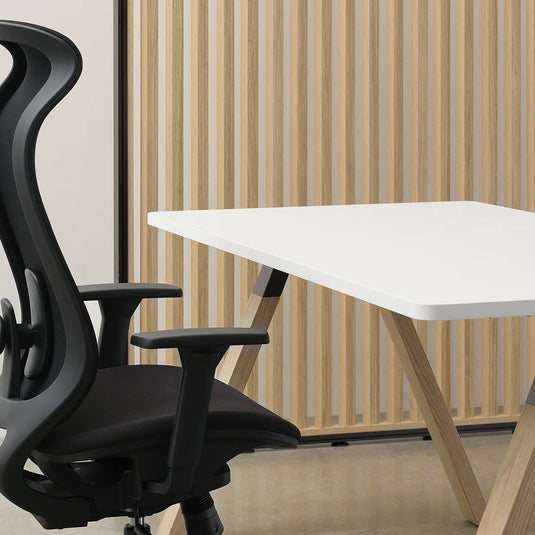 Black office chair next to a white desk with a wooden floor and wall in the background